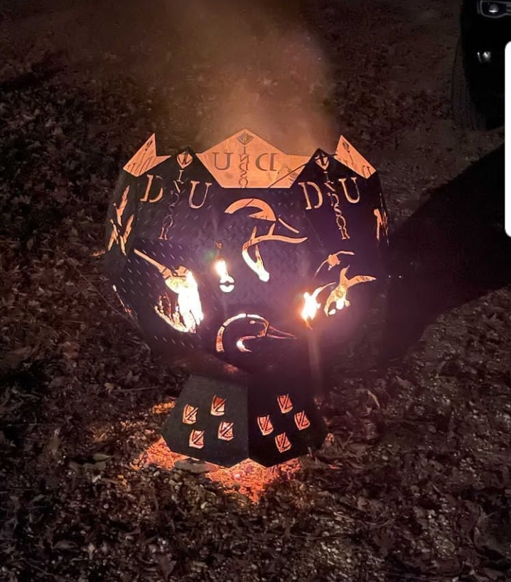 A patterned metal fire pit burning outdoors at night.