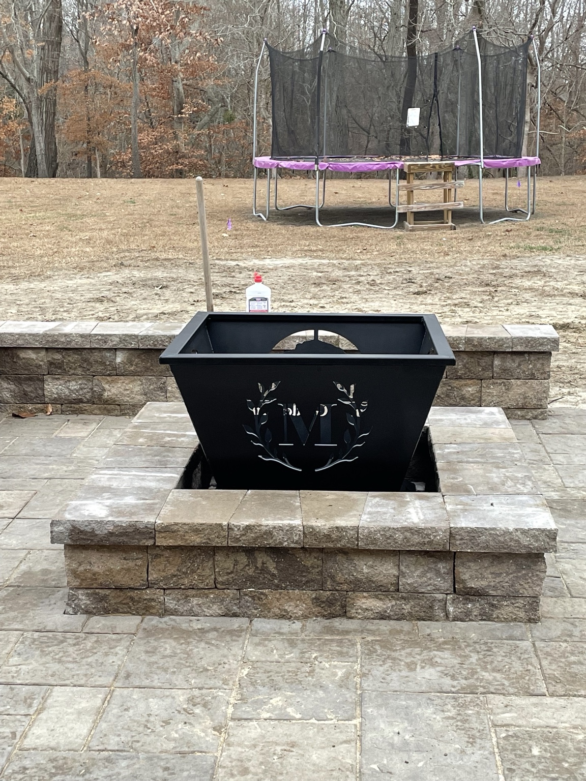 A square fire pit insert with deer artwork in a masonry surround.