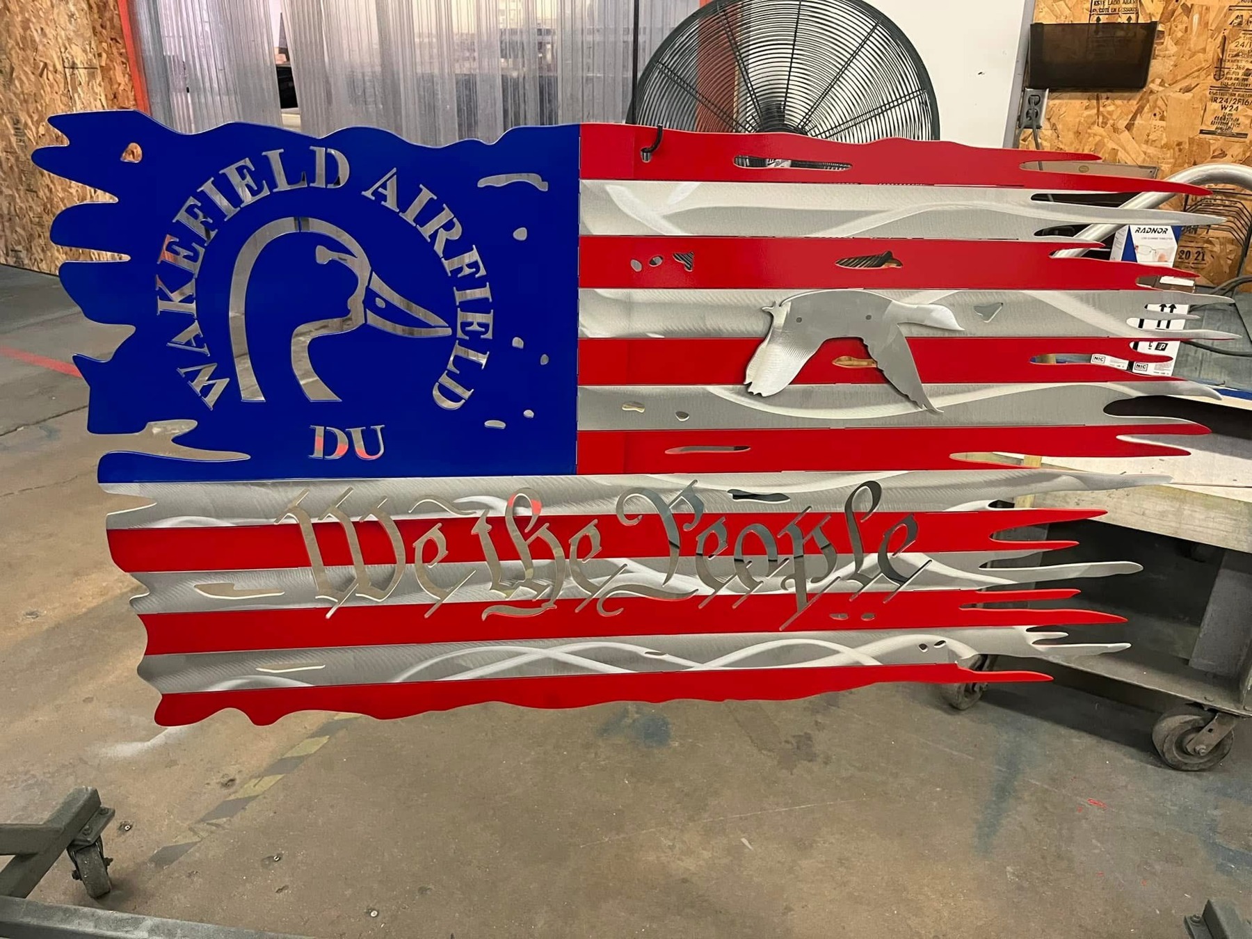 Custom red, white, and blue metal flag with Wakefield Airfield DU duck artwork and We the People lettering.
